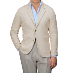 A person in a Sand Beige Summer Mouline Knitted Jacket by Maurizio Baldassari over a blue shirt with light gray pants stands against a plain background.