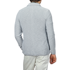 A person is shown from the back against a plain background, wearing a sky blue summer Mouline knitted jacket and white pants, highlighting the timeless elegance of Maurizio Baldassari's designs.