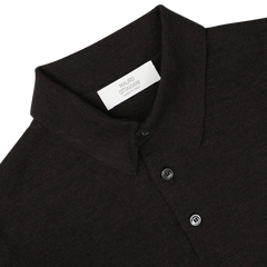 Close-up of a Mauro Ottaviani Brown Melange 16 Gauge Merino Wool Polo Shirt, featuring fine-knit long sleeves, a collar, and two buttons. A white label with text is visible inside the collar. The objects are set against a plain white background.