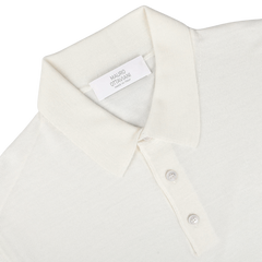 A Cream 16 Gauge Merino Wool Polo Shirt by Mauro Ottaviani is laid flat. The shirt has a plastic tag with the name "Mauro Ottaviani" and "Made in Italy" on it. The collar and three front buttons are clearly visible, showcasing its contemporary fit.