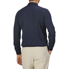 A person is standing with their back to the camera, wearing a Mauro Ottaviani Dark Blue 16 Gauge Merino Wool Polo Shirt and beige pants. The background is plain and light-colored.