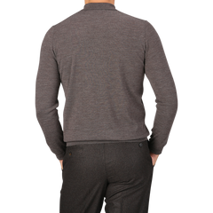 Rear view of a person wearing a long-sleeve, light brown 16 gauge Merino wool polo shirt by Mauro Ottaviani and dark gray trousers in a contemporary fit. The person is standing against a plain, light gray background.