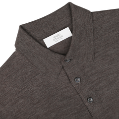 Close-up of a light brown collared, long-sleeve "Light Brown 16 Gauge Merino Wool Polo Shirt" by Mauro Ottaviani, with buttons and a white label featuring text.