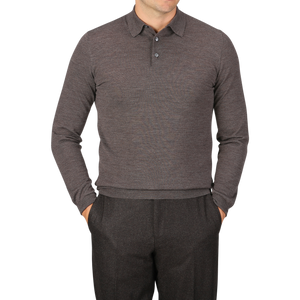 A person is wearing a long-sleeve, buttoned, light brown Mauro Ottaviani 16 gauge merino wool polo shirt and gray pants, with hands in pockets, standing against a gray background.