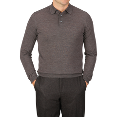 A person is wearing a long-sleeve, buttoned, light brown Mauro Ottaviani 16 gauge merino wool polo shirt and gray pants, with hands in pockets, standing against a gray background.