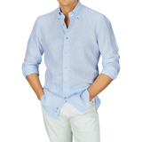 Man wearing a Mazzarelli Blue Striped Organic Linen BD Regular Fit Shirt, light blue button-up shirt and white pants with hands casually in pockets.