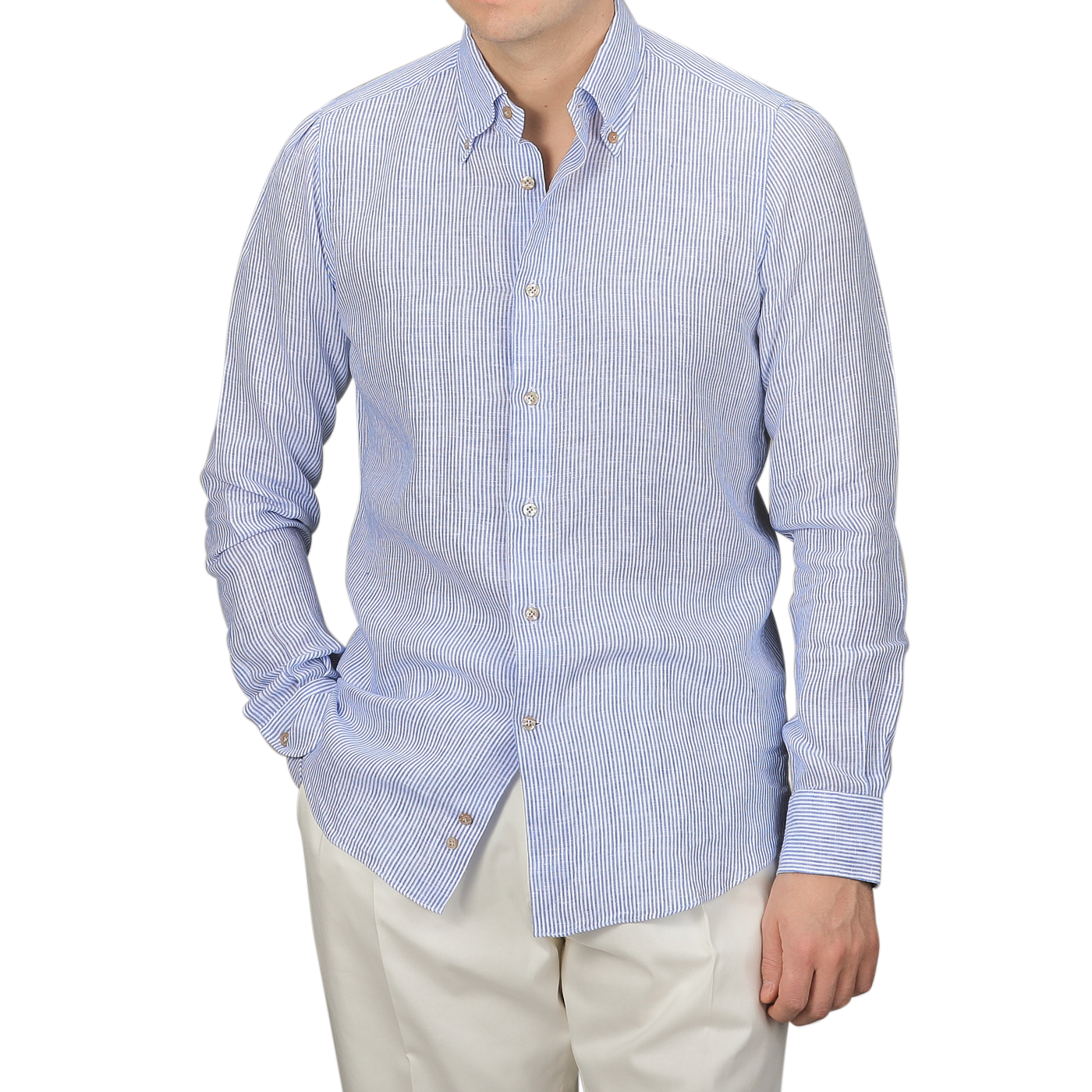 Wearing Mazzarelli's Blue Striped Organic Linen BD Shirt with the top button undone and paired with white pants, a person stands casually with one hand in their pocket.