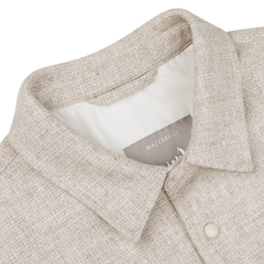 A close-up of a cream beige wool cashmere padded overshirt featuring a collar and button-down design on a white background, ideal for layering. The label reads "Mazzarelli.