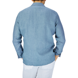 Rear view of a person wearing a Mazzarelli Indigo Blue Organic Linen Four Pocket Overshirt and white pants, standing against a plain light gray background.