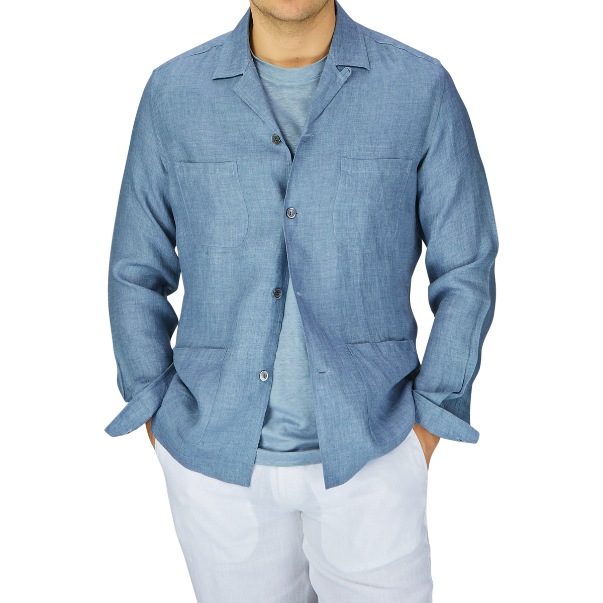 Man wearing a Mazzarelli Indigo Blue Organic Linen Four Pocket Overshirt over a white t-shirt with white pants, against a grey background.