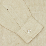 Close-up of a Mazzarelli khaki beige organic linen four pocket overshirtn cuff with a button, featuring a small brown stain near the sleeve placket.