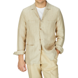 Man in a Khaki Beige Organic Linen Four Pocket Overshirt and matching pants by Mazzarelli, with a white t-shirt underneath, standing against a gray background.