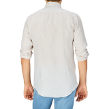 Rear view of a person wearing a light-colored, rolled-sleeve Mazzarelli Light Beige Organic Linen BD Slim Shirt and blue jeans against a grey background.