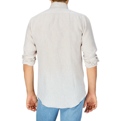 Rear view of a person wearing a light-colored, rolled-sleeve Mazzarelli Light Beige Organic Linen BD Slim Shirt and blue jeans against a grey background.