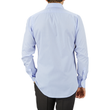 A man viewed from behind, wearing a Mazzarelli Light Blue Cotton Twill Cut Away Slim Shirt with a cutaway spread collar and dark trousers, standing against a neutral gray background.