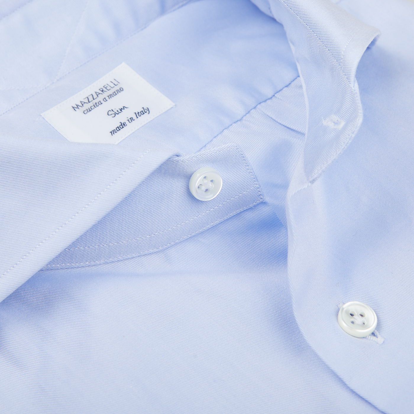 Close-up of a light blue Mazzarelli Light Blue Cotton Twill Cut Away Slim Shirt, focusing on the cutaway spread collar label reading "MAZZARELLI Classic Fit made in Italy" and two white buttons.