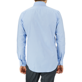 Rear view of a man wearing a Mazzarelli Light Blue Royal Oxford BD Slim Shirt and dark trousers, standing against a gray background.