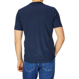 Rear view of a man wearing a Mazzarelli Navy Blue Merino Wool T-Shirt and blue denim jeans, standing against a light gray background.