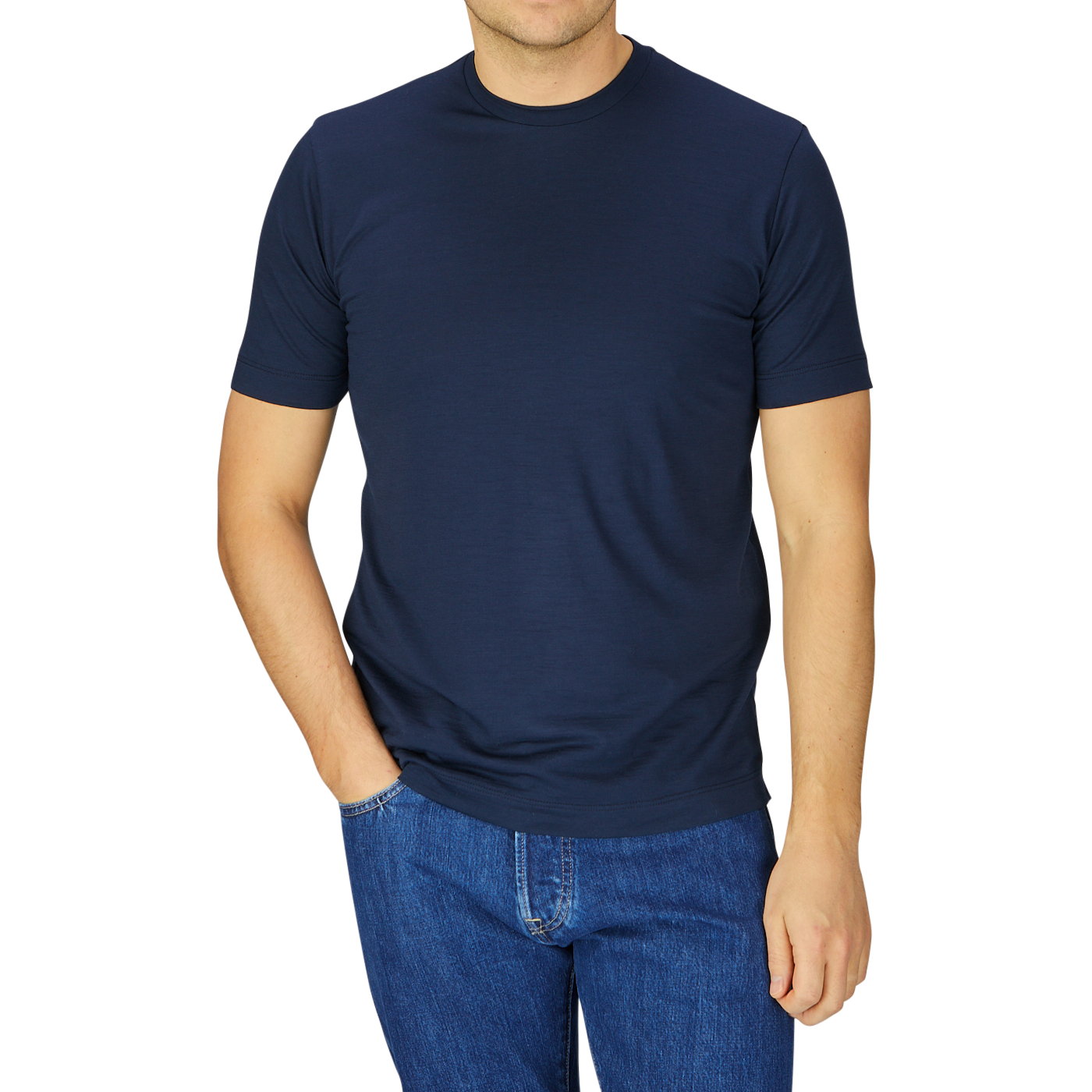 Man wearing a Mazzarelli navy blue merino wool T-shirt and blue jeans, standing with one hand slightly tucked in his pocket, against a striped grey background.
