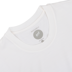 Close-up of a white, breathable merino wool t-shirt's neckline tagged with the brand "mazzarelli" in a circular, gray label.