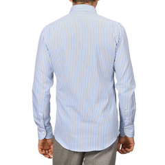 Rear view of an individual wearing the Mazzarelli White Blue Bengal Striped BD Slim Shirt, showcasing its light blue and white striped design in pinpoint cotton with hand-stitched pleated shoulders, complemented by gray pants against a plain background.