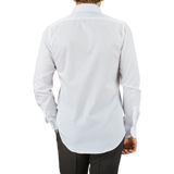 A man viewed from behind, wearing an untucked Mazzarelli White Cotton Twill Cutaway Slim Shirt and dark trousers against a gray background.