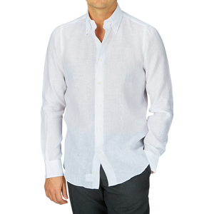 A man wearing a Mazzarelli White Organic Linen BD Slim Shirt and dark trousers against a gray background.