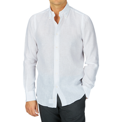 A man wearing a Mazzarelli White Organic Linen BD Slim Shirt and dark trousers against a gray background.