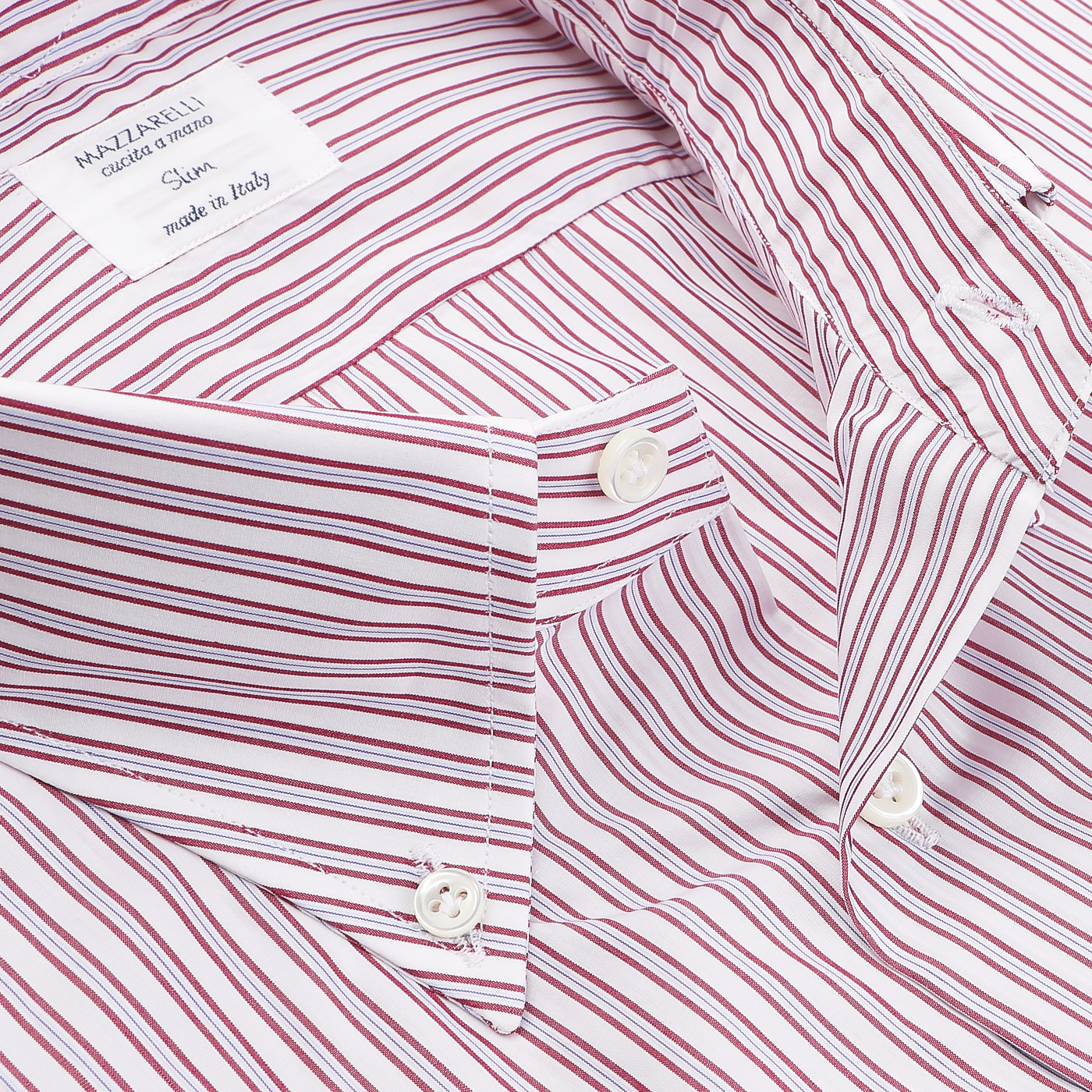 Here is a close-up of the White Red Vintage Striped Cotton BD Slim Shirt, designed by Mazzarelli. This vintage striped shirt, featuring thin red stripes on pure cotton twill, includes a soft button-down collar. It is labeled "made in Italy," with striking black buttons contrasting against the crisp fabric.