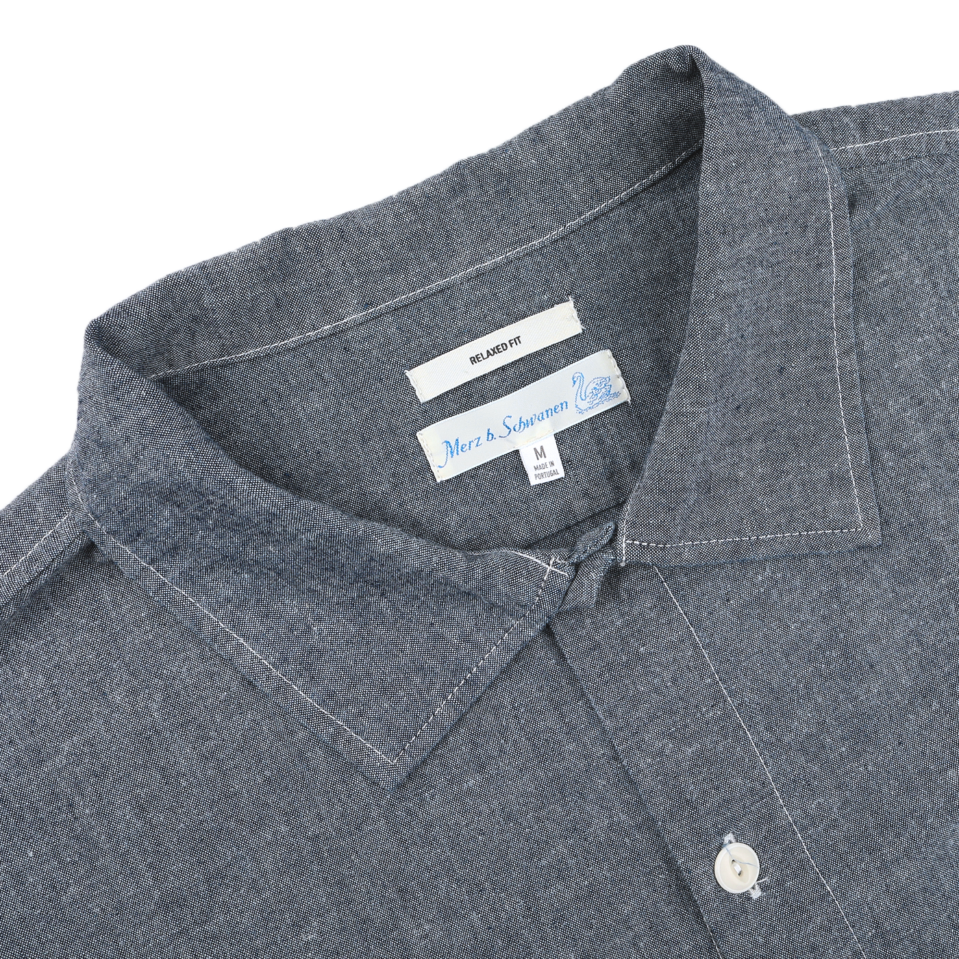 Close-up of the Denim Blue Cotton Chambrey 06 CH Shirt by Merz b. Schwanen, featuring a visible collar and brand label, made from organic cotton for an eco-friendly touch.