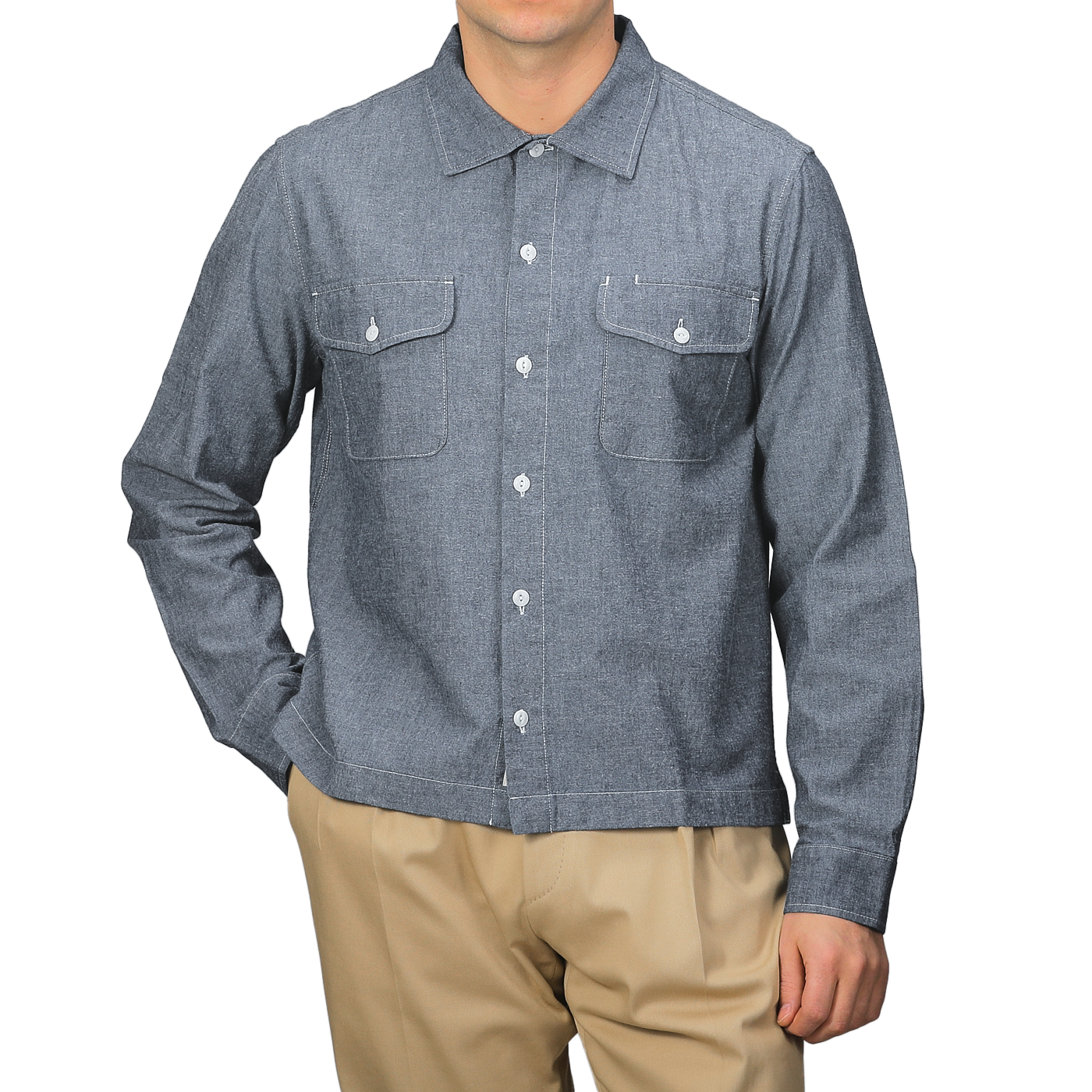 A person stands against a plain background wearing the Merz b. Schwanen Denim Blue Cotton Chambray 06 CH Shirt with two chest pockets and beige pants, showcasing its organic cotton composition for a sustainable yet stylish look.