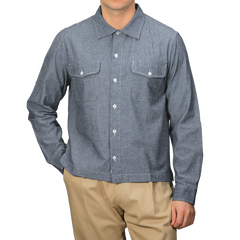 A person stands against a plain background wearing the Merz b. Schwanen Denim Blue Cotton Chambray 06 CH Shirt with two chest pockets and beige pants, showcasing its organic cotton composition for a sustainable yet stylish look.