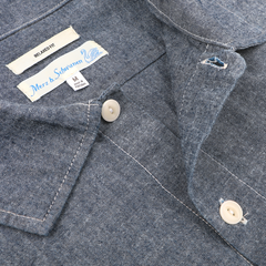 Close-up of a Denim Blue Cotton Chambray 06 CH shirt by Merz b. Schwanen, featuring labels "Relaxed Fit" and size "M," showcasing its organic cotton fabric and stonewashed finish.