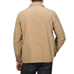 A person wearing a Khaki Beige Cotton Poplin 02 Jacket by Merz b. Schwanen, featuring vegan corozo buttons, and dark jeans stands with their back to the camera against a gray background.