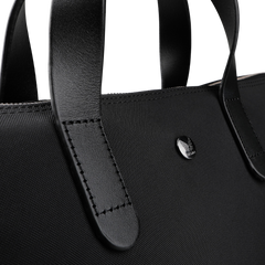 Close-up of the Eclipse Black M/S Nylon Brief by Mismo, an urban handbag crafted from ballistic nylon with sturdy leather handles and a small circular metal emblem.