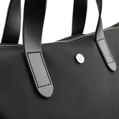 The Eclipse Black M/S Nylon Shopper by Mismo is an urban tote made from waterproof ballistic nylon, featuring sturdy full-grain leather handles, a visible zipper, and a small round metal emblem with an engraved logo—perfect for style and durability.