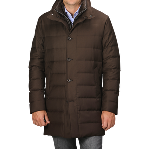 A person wearing a dark brown, Montecore Brown Super 120s Wool Batavia Padded Coat featuring buttons stands against a grey background. The Italian outerwear boasts a high collar and is paired with blue jeans.