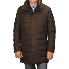 A person wearing a dark brown, Montecore Brown Super 120s Wool Batavia Padded Coat featuring buttons stands against a grey background. The Italian outerwear boasts a high collar and is paired with blue jeans.