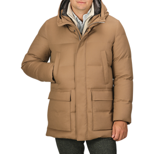 A person wearing the Camel Beige VBC Wool Flannel Padded Parka with a high collar and hood, placing one hand in a front pocket. This stylish piece from Italian outerwear specialist Montecore seamlessly blends functionality with sophistication.