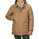 A person wearing the Camel Beige VBC Wool Flannel Padded Parka with a high collar and hood, placing one hand in a front pocket. This stylish piece from Italian outerwear specialist Montecore seamlessly blends functionality with sophistication.