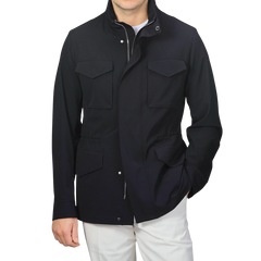 Wearing a Montecore Midnight Blue Aéro Twill Field Jacket made of technical nylon with four front pockets and white pants, a person stands against a plain background.