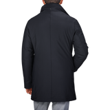 Back view of a person wearing a navy blue Montecore nylon technical padded car coat with a standing collar and grey pants.