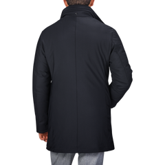 Back view of a person wearing a navy blue Montecore nylon technical padded car coat with a standing collar and grey pants.