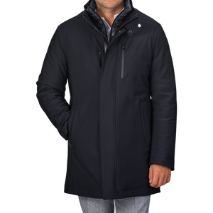 Rewritten Sentence:
A man in a Montecore Navy Blue Nylon Technical Padded Car Coat with a high collar and gray pants is standing with one hand in his pocket. The padded car coat features a front zipper, snap buttons, and a vertical chest pocket. The man's face is not visible.