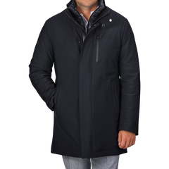 Rewritten Sentence:
A man in a Montecore Navy Blue Nylon Technical Padded Car Coat with a high collar and gray pants is standing with one hand in his pocket. The padded car coat features a front zipper, snap buttons, and a vertical chest pocket. The man's face is not visible.