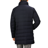 A person wearing a long, navy blue Montecore Super 120s Wool Batavia Padded Coat with a high collar, viewed from the back. The Italian outerwear features horizontal stitching and extends below the hips.