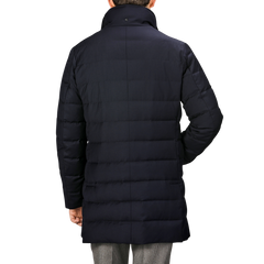 A person wearing a long, navy blue Montecore Super 120s Wool Batavia Padded Coat with a high collar, viewed from the back. The Italian outerwear features horizontal stitching and extends below the hips.