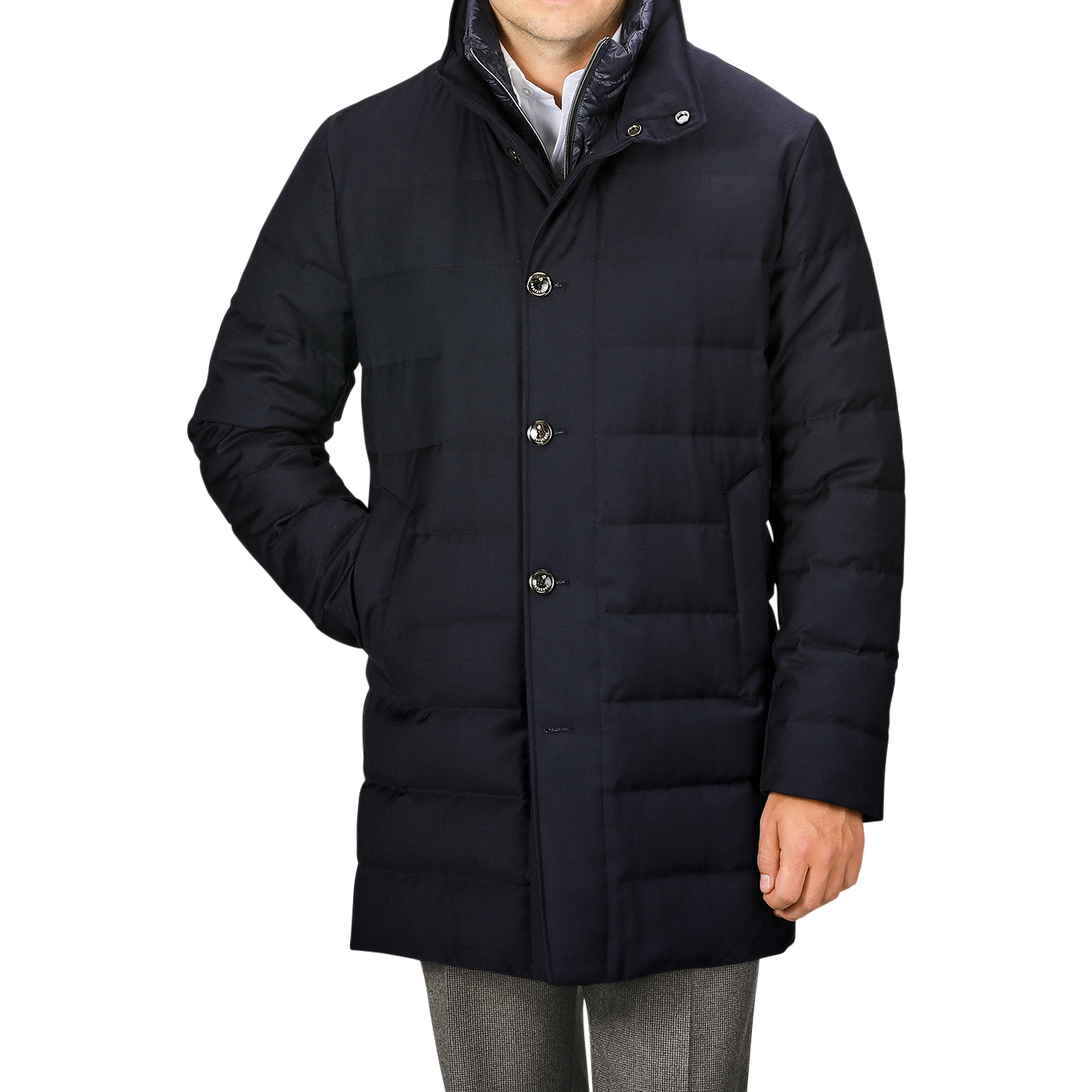 A person wearing a Navy Blue Super 120s Wool Batavia Padded Coat by Montecore, featuring a high collar and button-up design, paired with grey trousers, standing with one hand relaxed by their side.