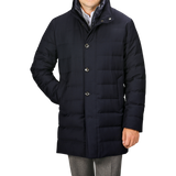 A person wearing a Navy Blue Super 120s Wool Batavia Padded Coat by Montecore, featuring a high collar and button-up design, paired with grey trousers, standing with one hand relaxed by their side.