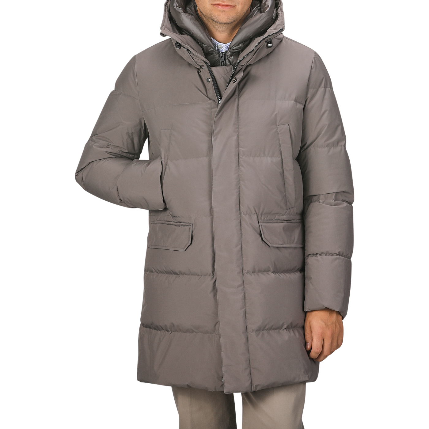 A man wearing the Taupe Beige Nylon Down Padded Parka by Montecore, which features knee-length padding, a front zipper, and two large front pockets, stands with one hand in a pocket.